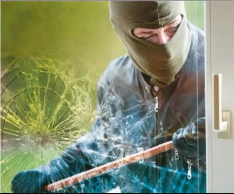Burglar breaking through commercial storefront glass — security film holds it in place
